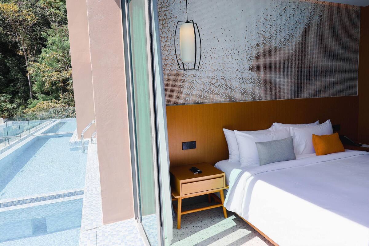 Une chambre d’hôtel avec un lit, une table de chevet et une vue sur une piscine et des arbres.