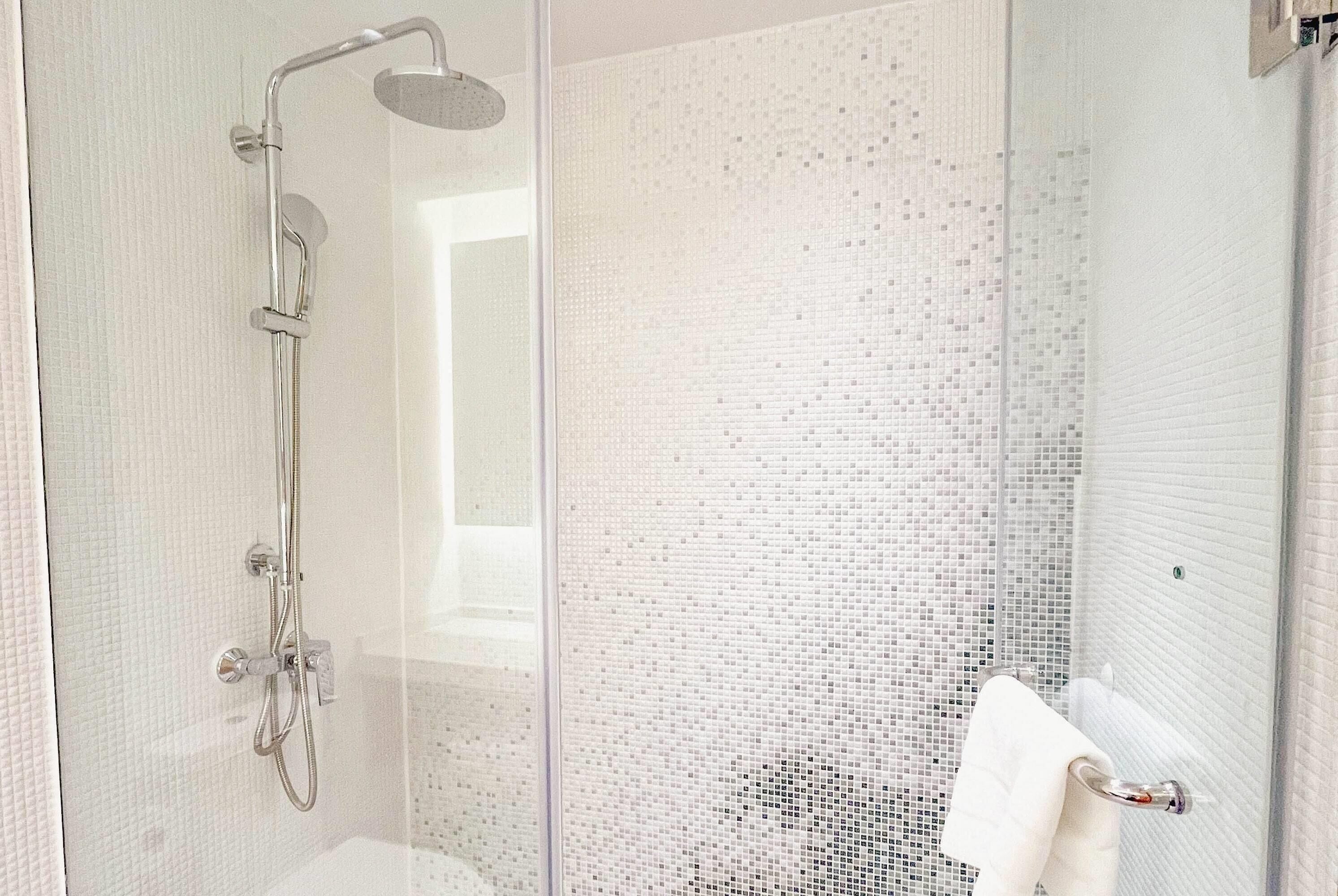 A modern shower with a glass door, a white tiled wall, and a visible towel rack.