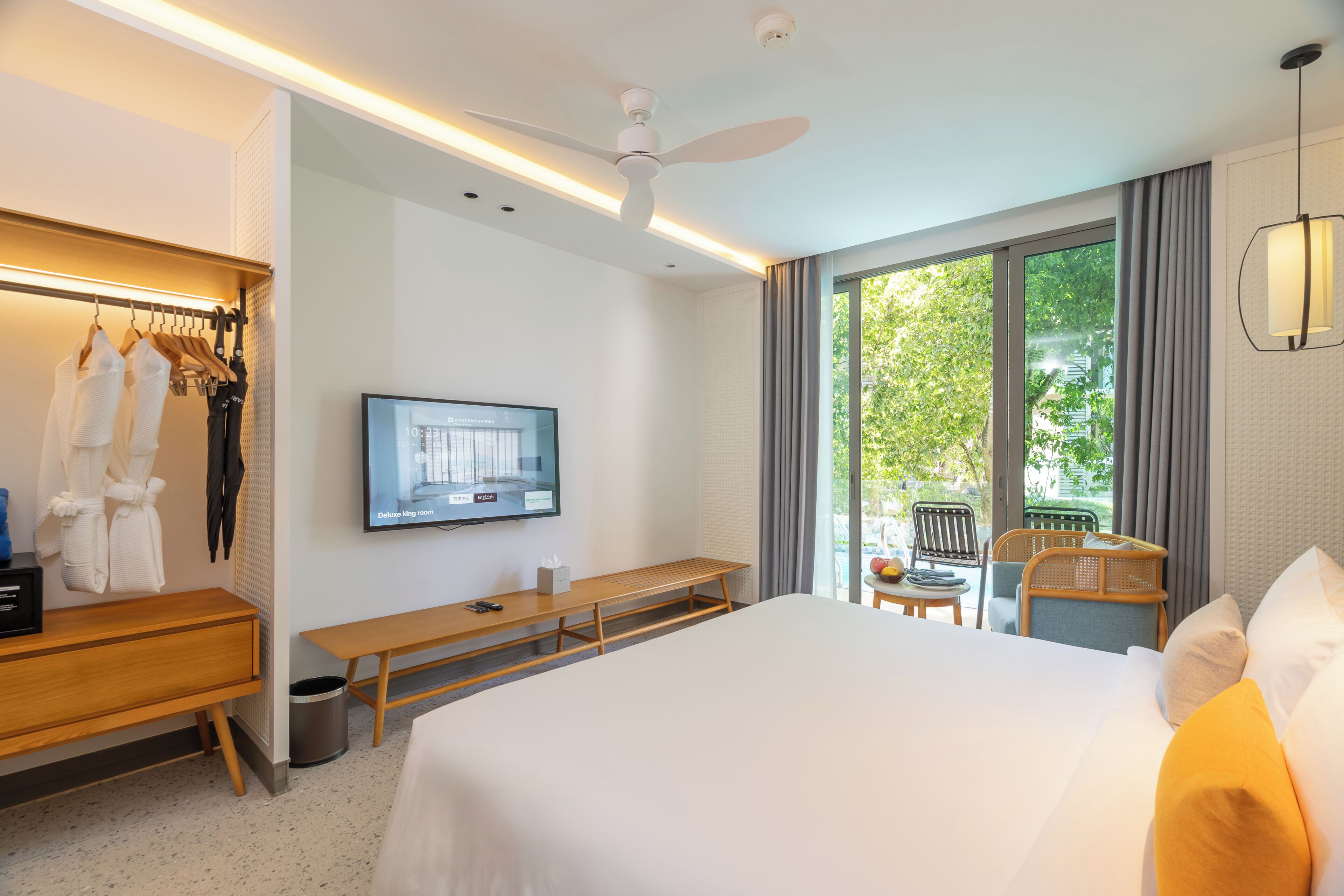 A hotel room with a bed, a TV, a desk, a bench, a chair, and a view of the outdoors.