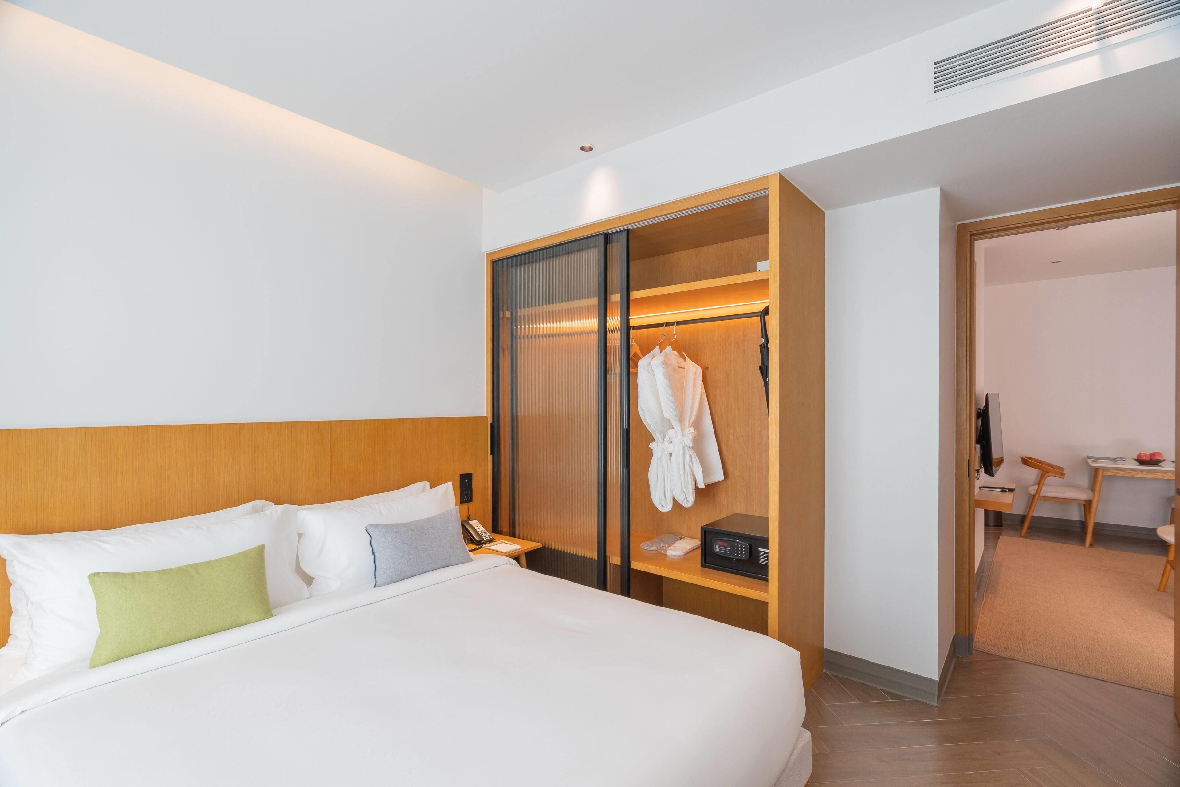 Een hotelkamer met een groot bed, een kledingkast met spiegel, een bureau met stoel en een kleine tafel met stoel.