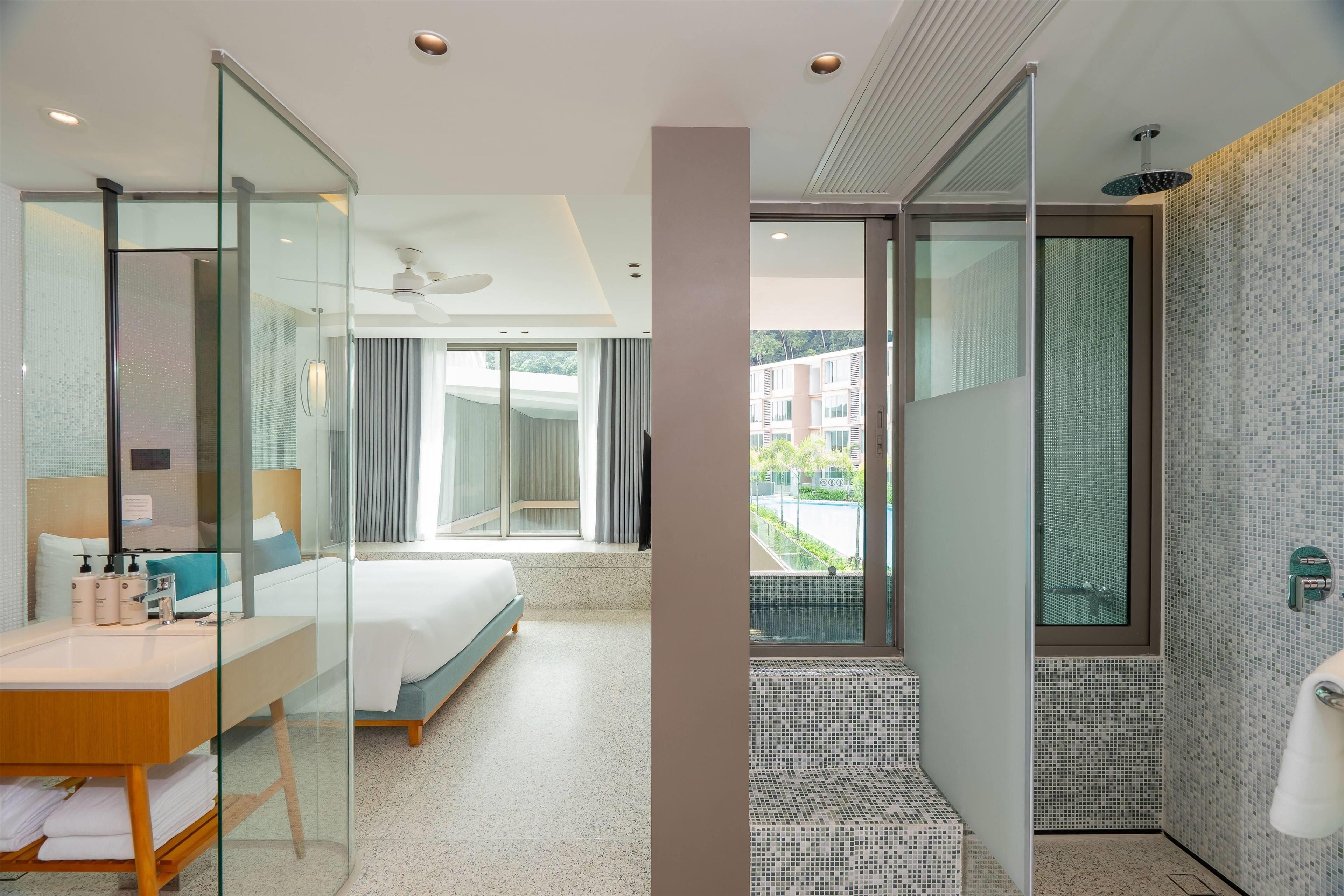 A modern hotel room with a glass partition, a bed, a bathroom with a shower, and a view of the outside.