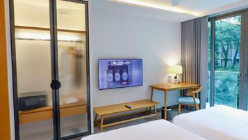 Habitación de hotel con cama, televisor montado en la pared, escritorio con lámpara y vistas al verdor exterior.