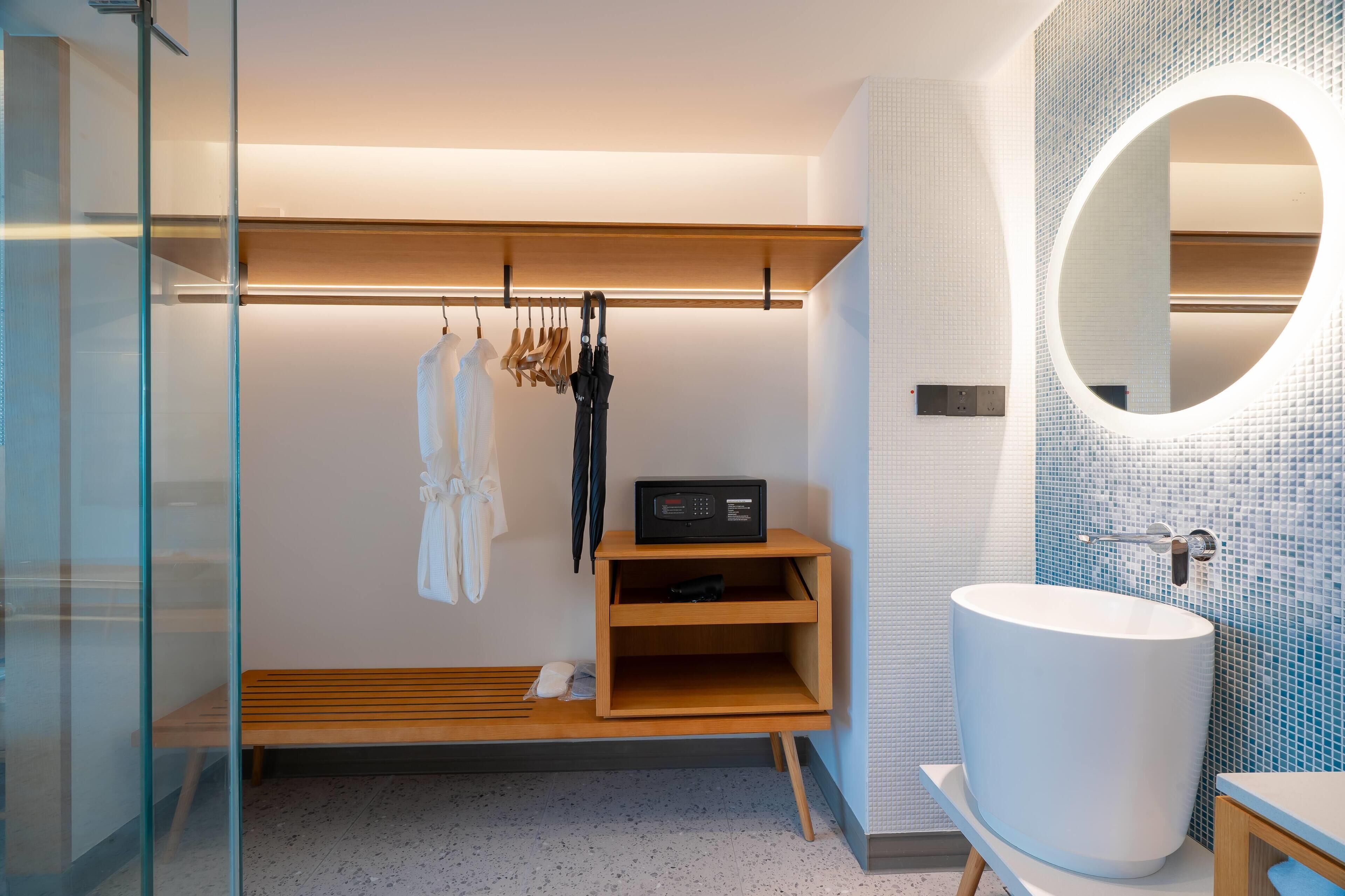 A modern bathroom with a large white sink, a wooden bench, a shelf with a radio, and a glass shower enclosure.