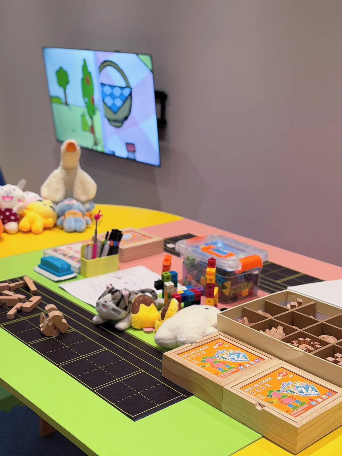 Una mesa con varios juguetes, bloques de construcción y un televisor que muestra una caricatura.