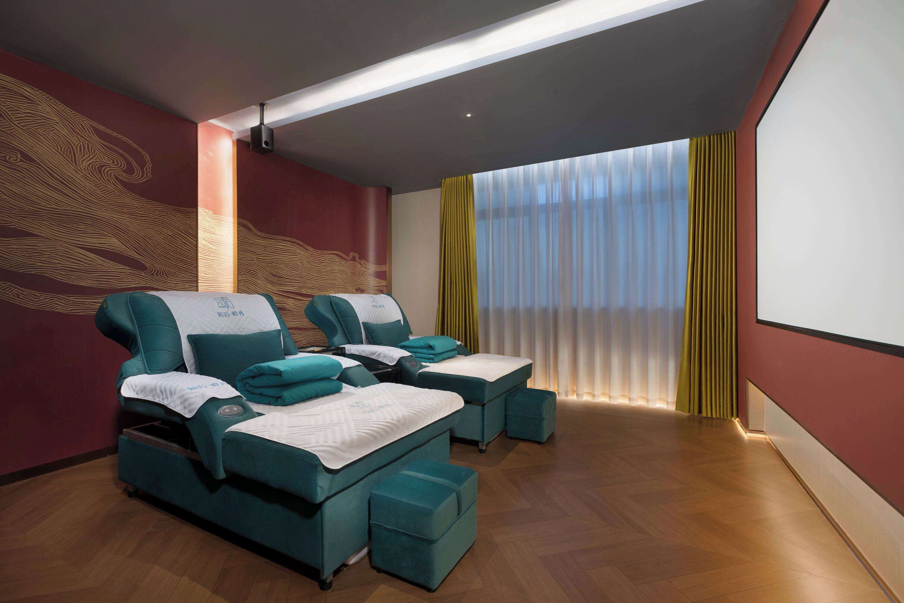 A room with two massage therapy beds, a large screen, and a window with curtains.