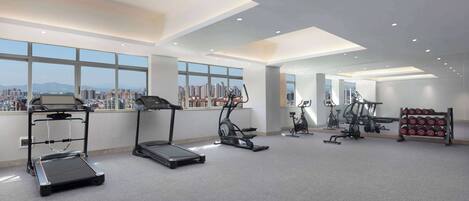 A modern gym with treadmills, an elliptical, and a rack of dumbbells.