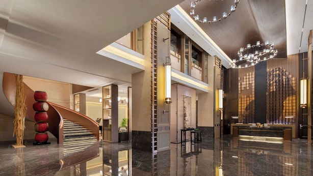 A spacious lobby with a curved staircase, a reception desk, and a modern chandelier.