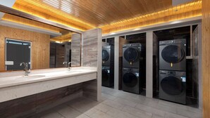 A modern bathroom with a wooden ceiling, a large mirror, a sink, and multiple washing machines.