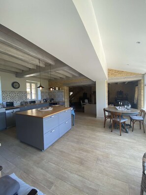 A spacious kitchen with a large island, wooden flooring, and a dining area with a round table and chairs.