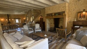 A spacious living room with a high ceiling, exposed beams, a fireplace, and a staircase leading to an upper level.
