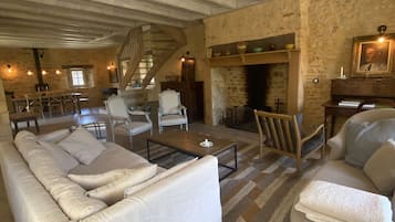 A spacious living room with a high ceiling, exposed beams, a fireplace, and a staircase leading to an upper level.