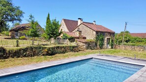 A stone house with a tiled roof, a swimming pool, and a wooden fence.