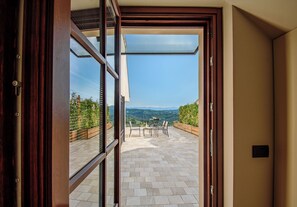 Una vista attraverso una porta vetrata su un patio con tavolo e sedie, una recinzione in legno e un paesaggio montuoso.