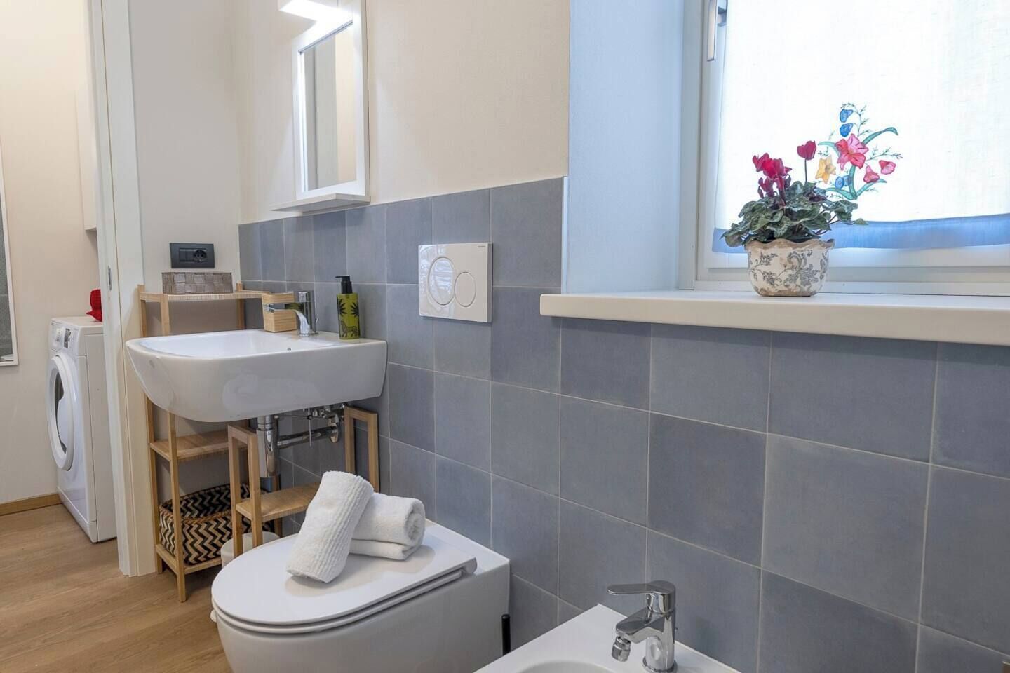 A modern bathroom with a white sink, a toilet, and a window with a potted plant.