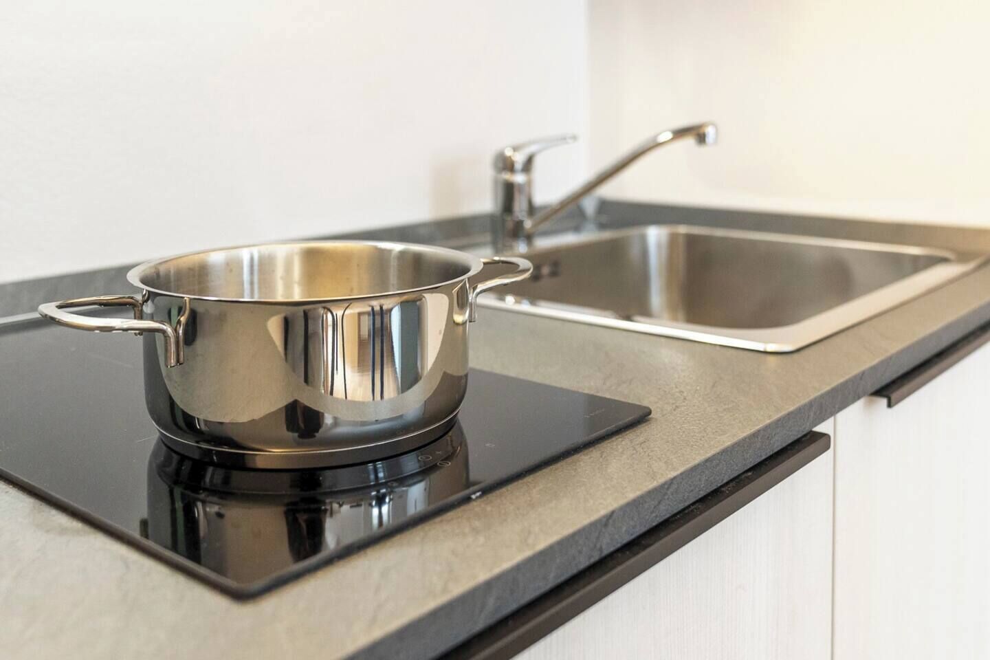 A stainless steel pot on an induction cooktop next to a modern kitchen sink.