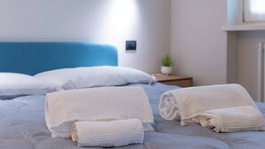 A neatly made bed with white linens and rolled towels, a blue headboard, a small bedside table with a plant, and a wall-mounted light fixture. - Elegant Panoramic Two-room Apartment. Treiso Belvedere Elegance, Elegant Panoramic Two Bedroom Apartment. Treiso Belved... (Treiso)
