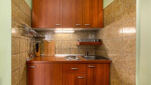 A compact kitchen with wooden cabinets, a stainless steel sink, and a tiled backsplash. - Stunning apartment in Palit with WiFi (Palit)