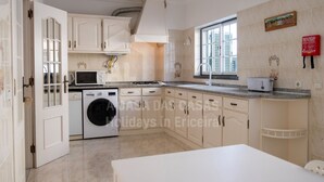 A modern kitchen with white cabinets, a washing machine, a microwave, and a toaster. - Casa os Naias by ACasaDasCasas (Ericeira)