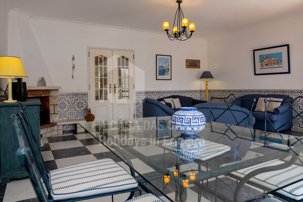 A living room with a glass coffee table, blue sofa, patterned tiles, and a chandelier.