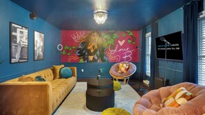 A modern living room with a vibrant mural, a tufted sofa, a round coffee table, and a comfortable armchair. - 8 Beds, Large Groups, Karaoke, Firepit  (Charlotte)
