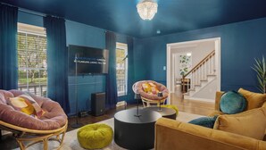A living room with a blue wall, a television, a piano, and a staircase leading to another room. - 8 Beds, Large Groups, Karaoke, Firepit  (Charlotte)