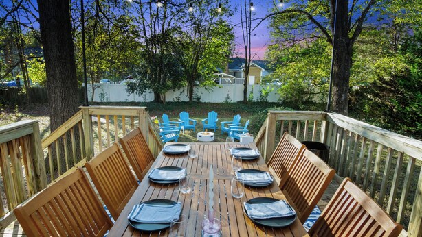 An outdoor dining area with wooden benches and blue Adirondack chairs, surrounded by trees and a white fence. - 8 Beds, Large Groups, Karaoke, Firepit  (Charlotte)
