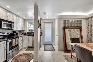 Una cocina moderna con armarios blancos, electrodomésticos de acero inoxidable y un comedor con mesa y sillas.