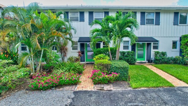 A two-story building with a green door, surrounded by lush greenery and a paved pathway. - Magnificent Beach Townhome Steps from Atlantic Ave (Delray Beach)
