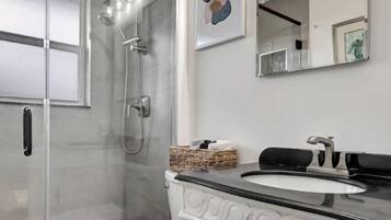 Une salle de bain moderne avec une douche à parois de verre, des toilettes blanches et un meuble-lavabo doté d’un plan de travail noir.