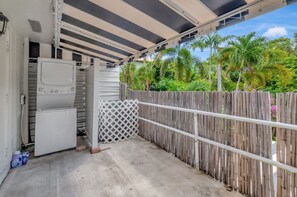 Un espace extérieur abrité, avec un réfrigérateur blanc, une clôture en bois et un treillage.