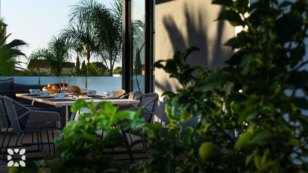 Un área de comedor al aire libre con una mesa dispuesta para dos personas, rodeada de sillas de mimbre.