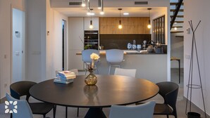 Una cocina moderna con armarios de madera, una zona de comedor con una mesa y sillas redondas, e iluminación colgante.