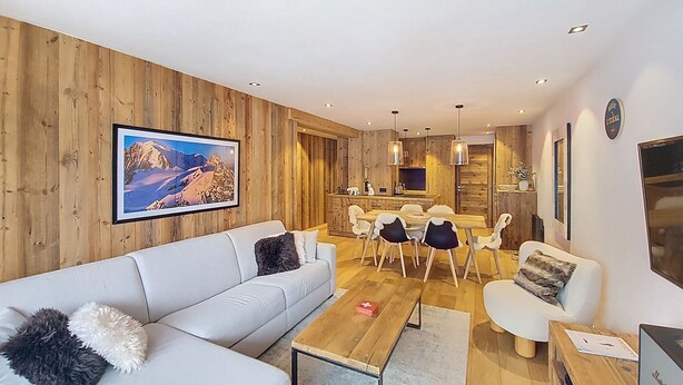 Een moderne woonkamer met een houten wand, een groot lijstwerk, een bank en een eethoek met stoelen en een tafel.