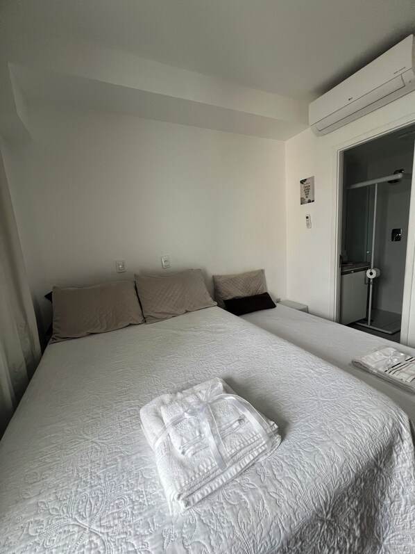 Habitación de hotel con una cama grande, un baño con puerta de vidrio y una mesita con una toalla.