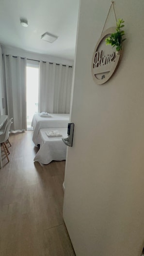 Quarto de hotel com cama, escrivaninha e cadeira. Placa na parede com a palavra 'Home'.