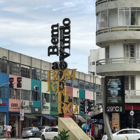 A street scene with a prominent sign reading 'Bom ao BEM' and a large building with multiple windows and balconies.