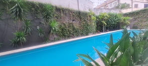 Piscina cercada por vegetação exuberante e um muro de concreto.