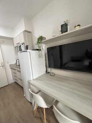 Una cocina moderna con armarios blancos, microondas integrado y un televisor de pantalla plana grande montado sobre una encimera de madera.