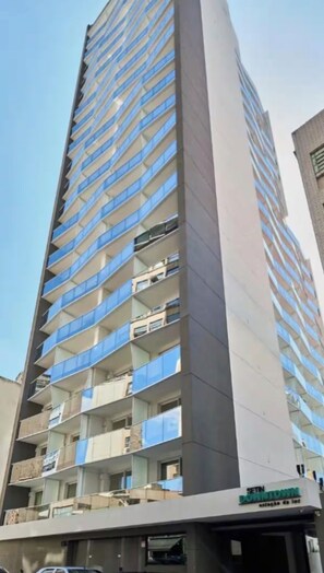 Un edificio de varios pisos con balcones, una entrada visible y un letrero que indica un uso comercial.