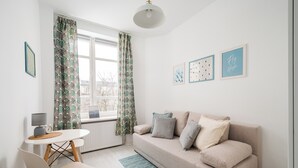 Una sala de estar moderna con un sofá color beige, una mesita, un sillón y una ventana con cortinas estampadas.