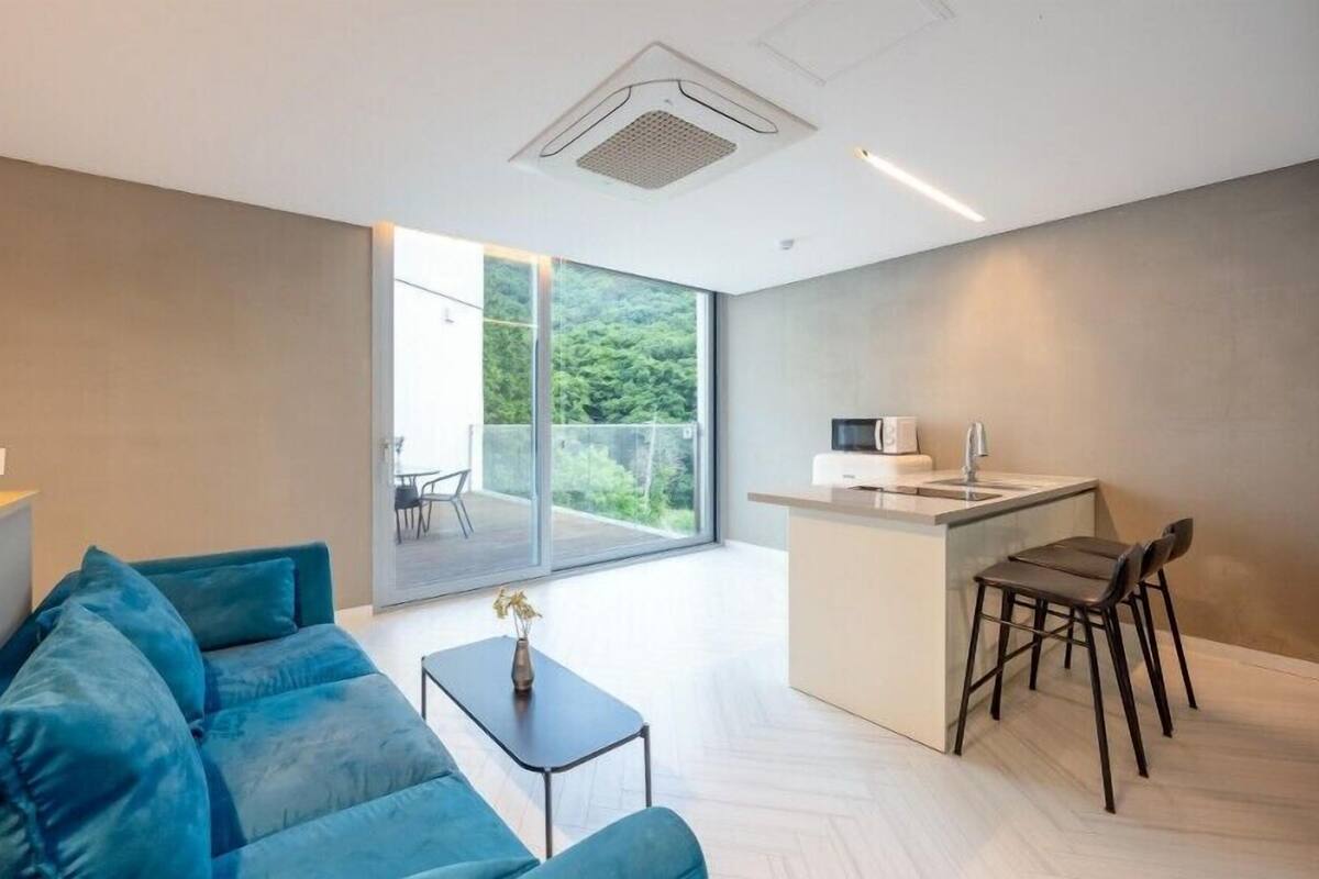A modern living room with a blue sofa, a small table, and a kitchen area with a sink and chairs.