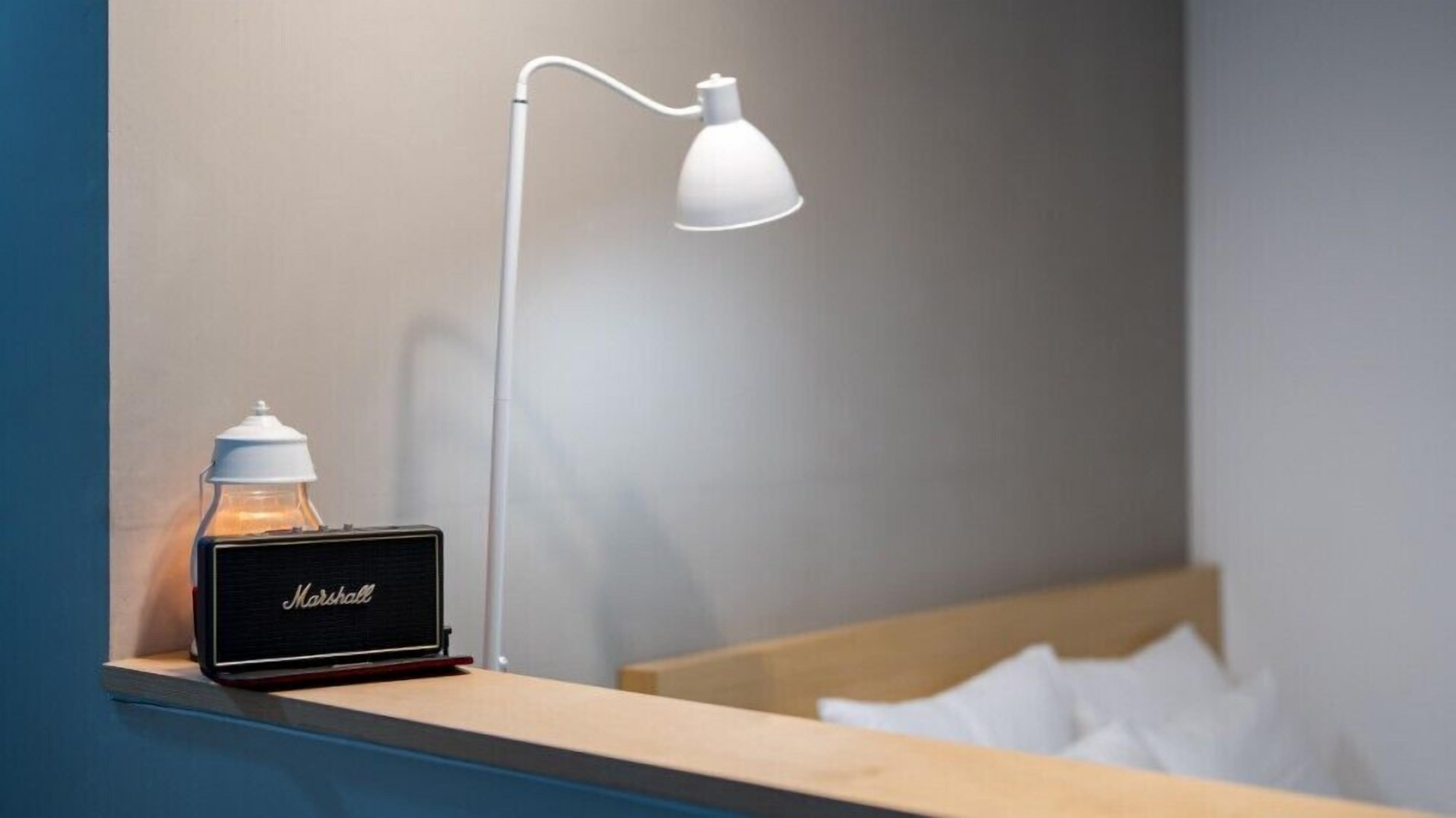 A bedside table with a Marshall speaker and a white desk lamp.
