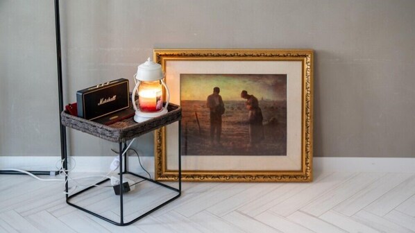 A framed painting on a wall, a small table with a lamp and a radio, and a power cord on the floor. - west side (Tongyeong)