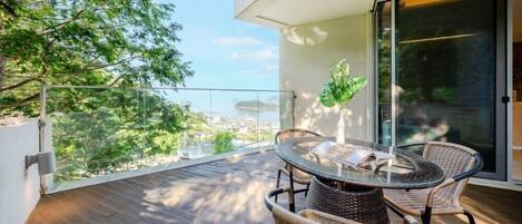 Ein Balkon mit Korbstühlen und einem Tisch, der auf eine Stadtansicht und ein Gewässer blickt.