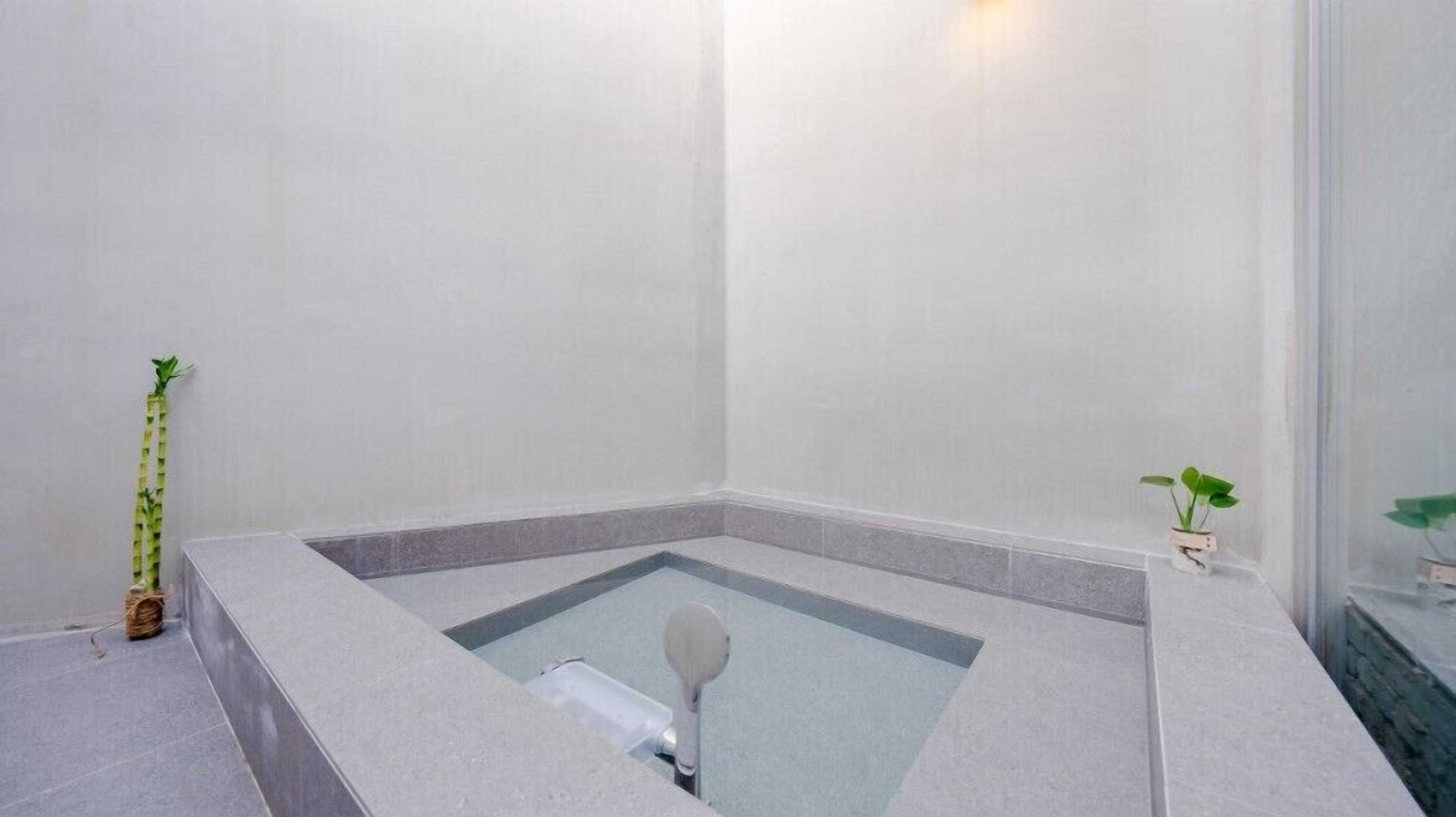 A modern bathroom with a built-in bathtub, a small window, and a potted plant.