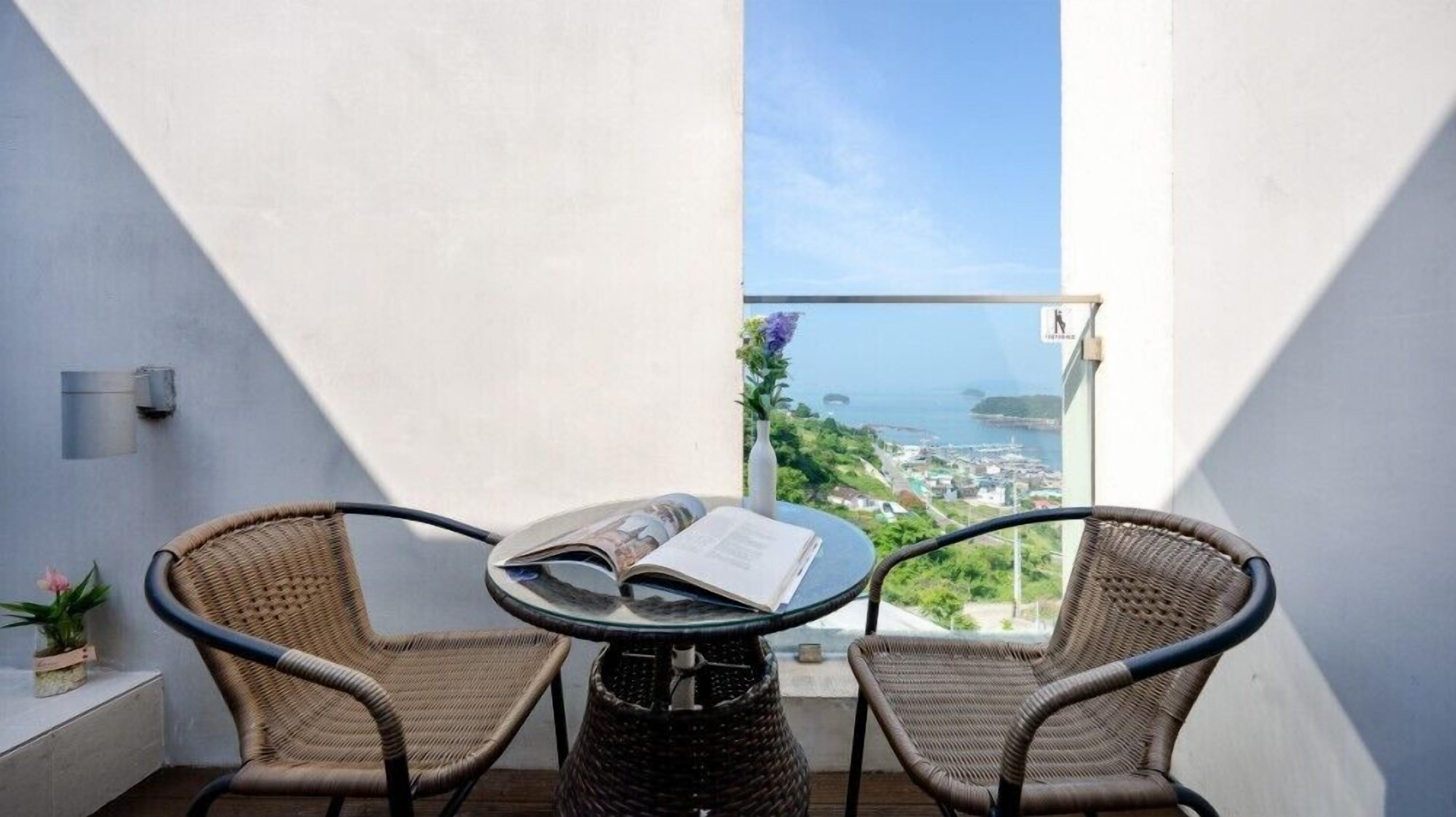 A balcony with two wicker chairs, a glass table, and an open book.