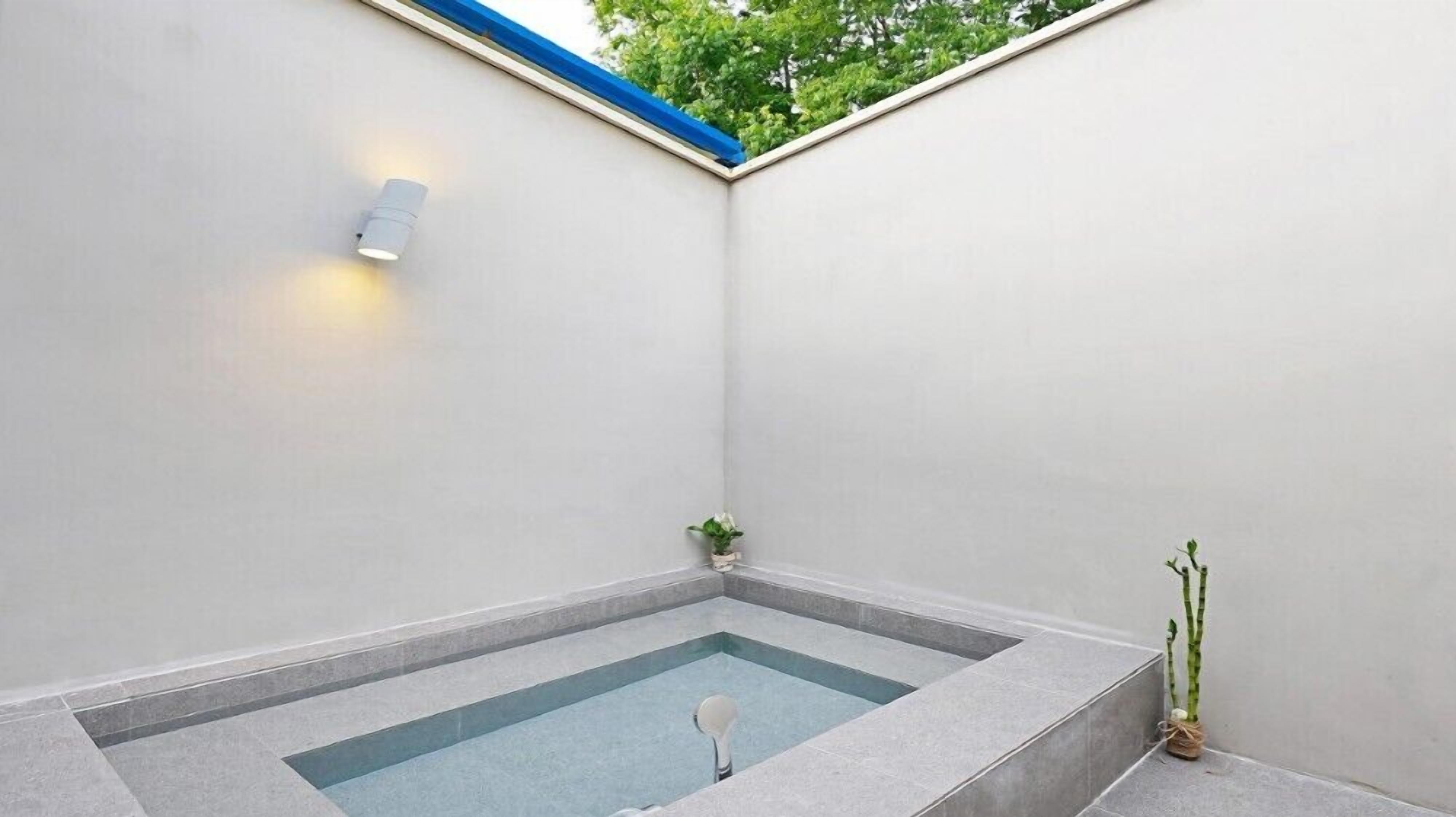 Une petite salle de bain moderne avec une baignoire intégrée, un luminaire fixé au mur et une plante en pot.