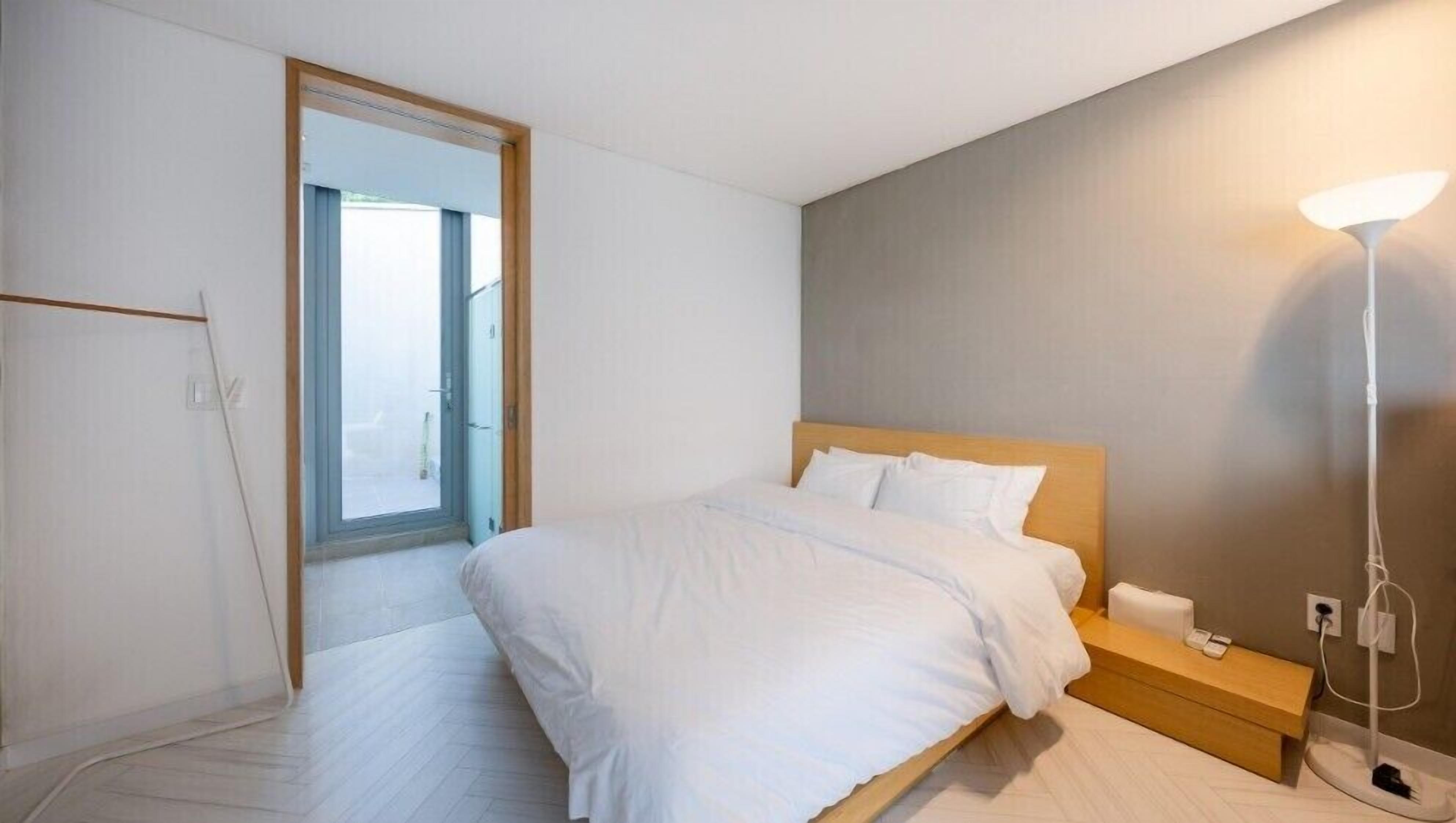 A bedroom with a bed, bedside table, lamp, and a door leading to a balcony.