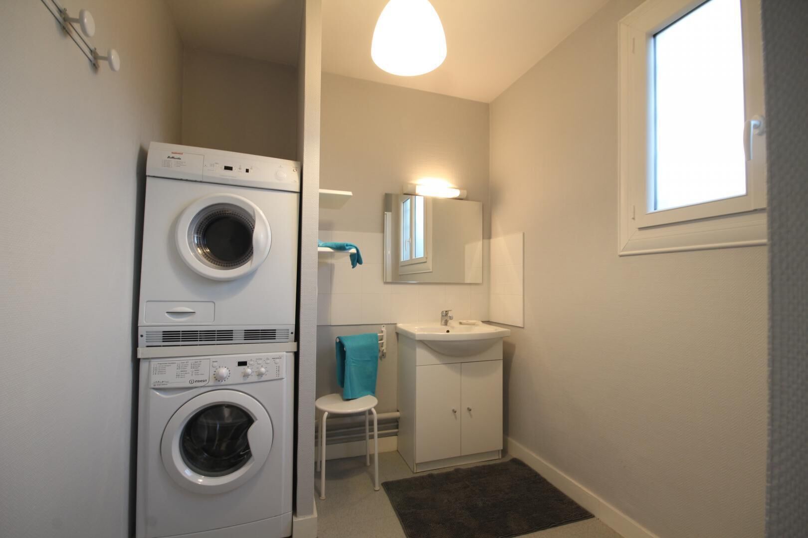 A compact laundry room with stacked washers and dryers, a small sink, and a mirror above it.