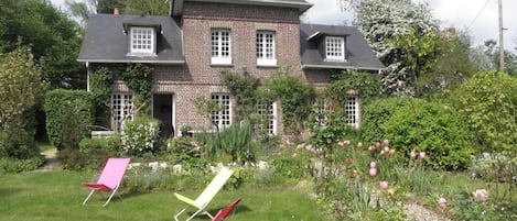 Et toetages murstenshus med have, tre liggestole og blomstrende blomster.